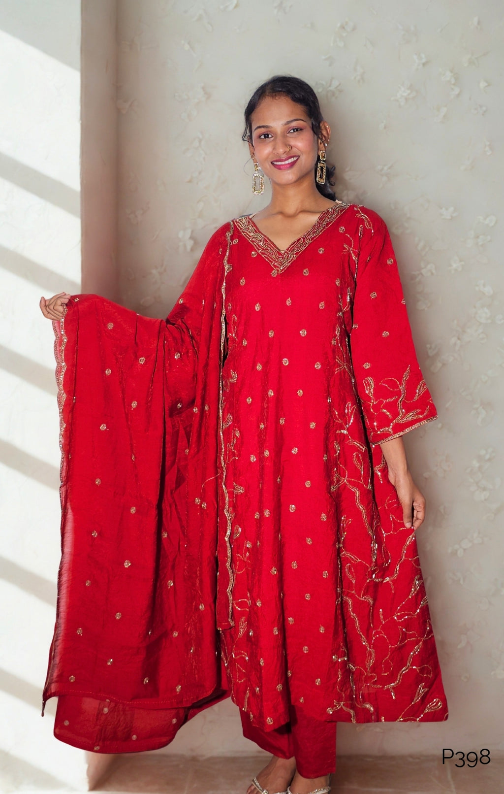 Woman wearing a red traditional outfit with gold embroidery against a neutral background