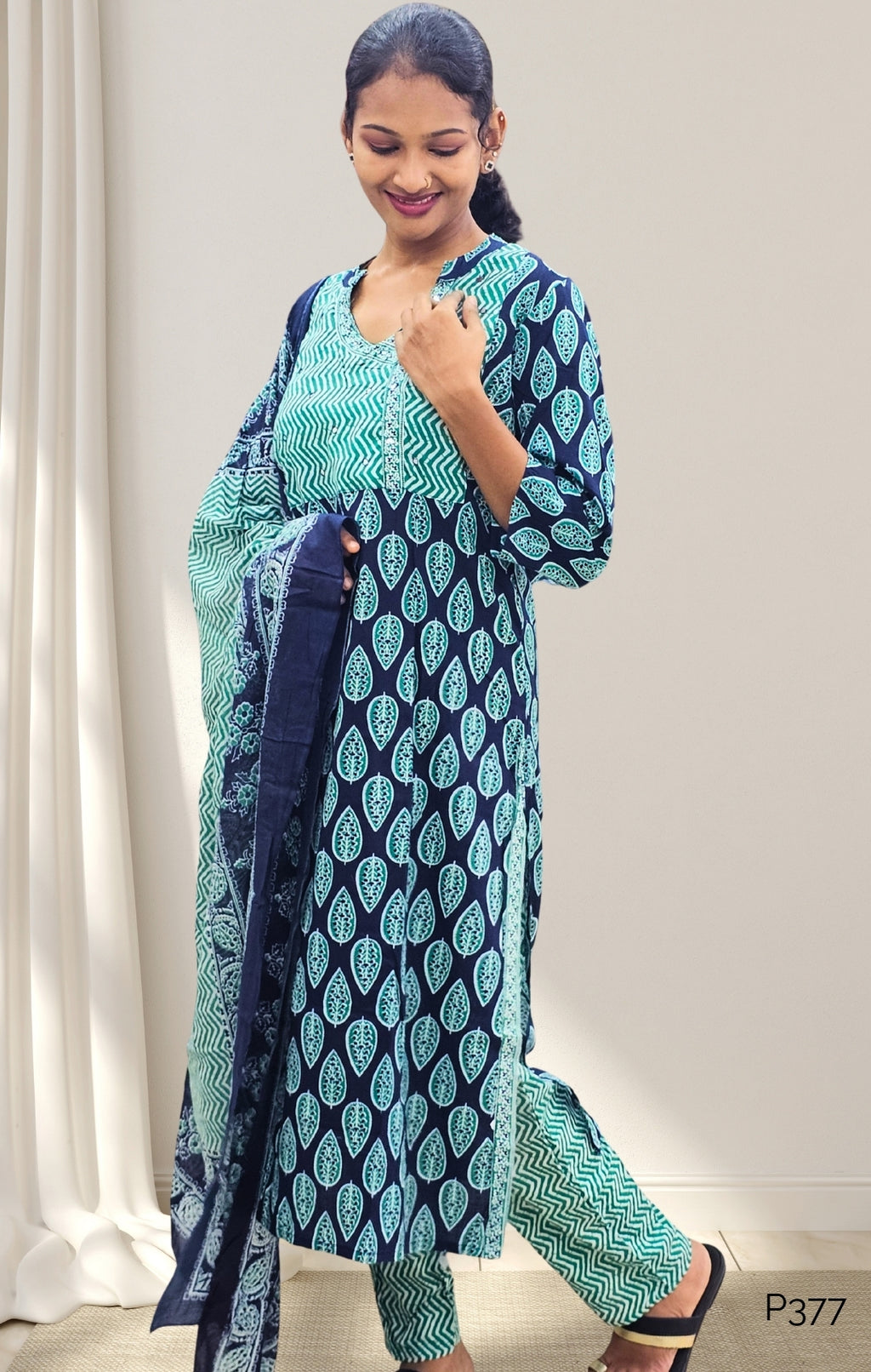 Woman wearing a blue and green traditional outfit with a white curtain background