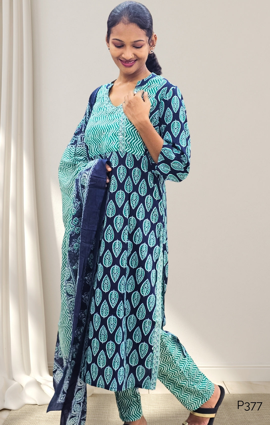 Woman wearing a blue and green traditional outfit with a white curtain background