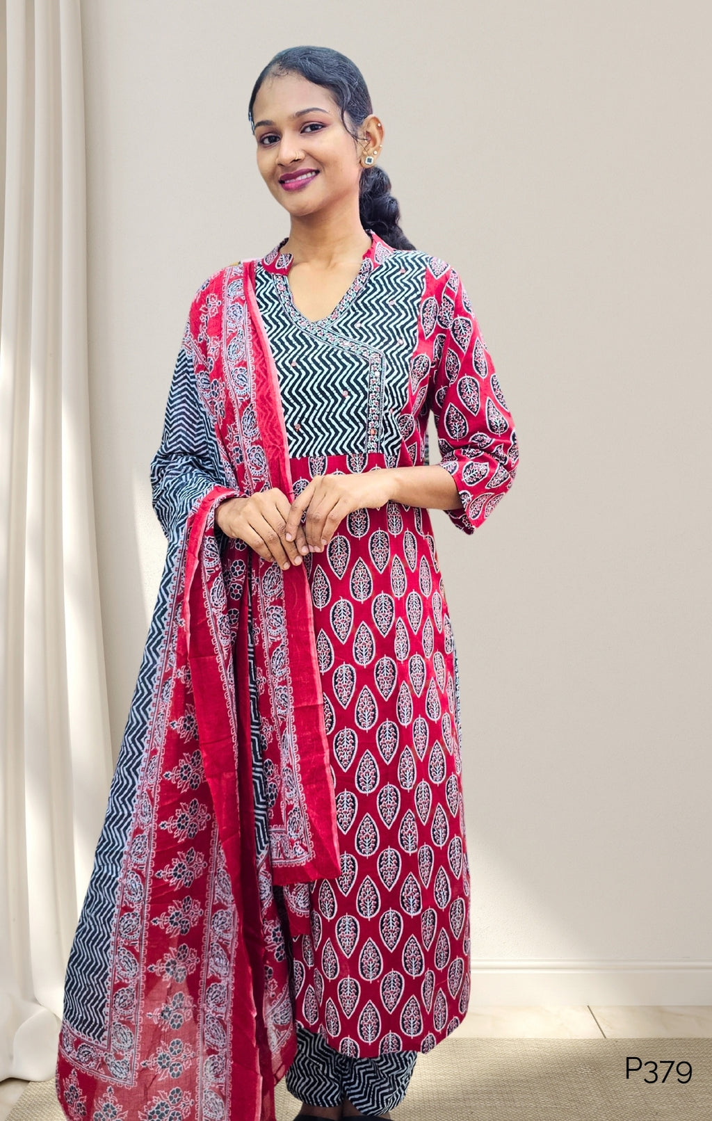 Woman wearing a red and black patterned outfit with a matching dupatta against a neutral background
