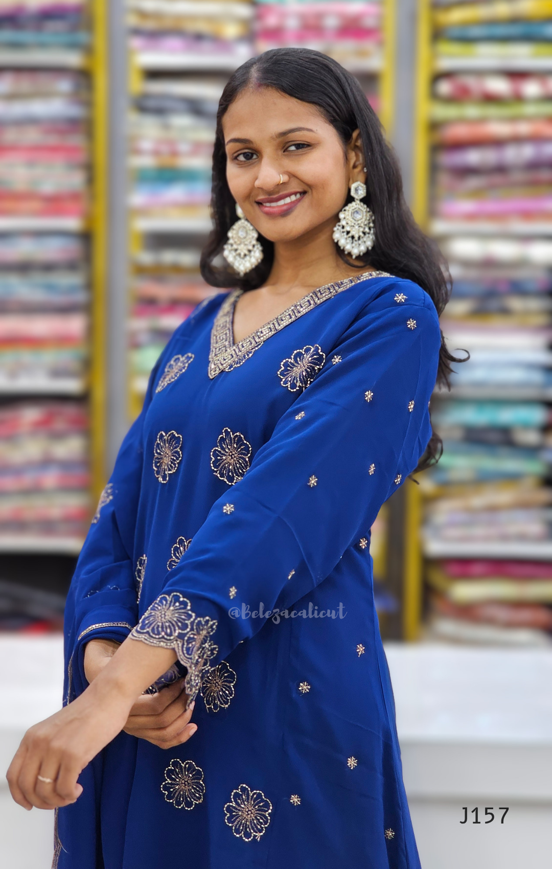 Woman wearing a blue embroidered outfit in front of fabric racks.