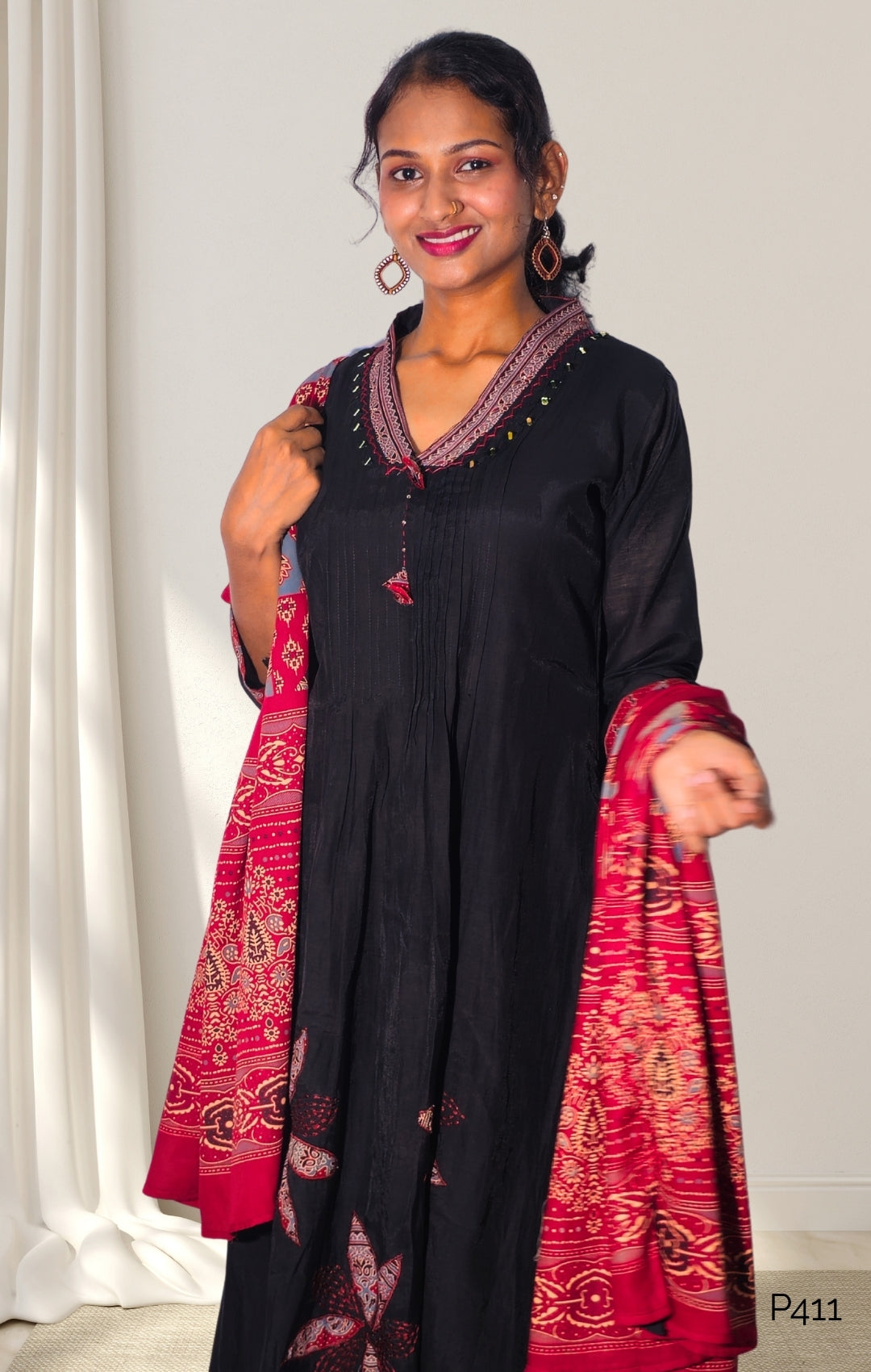Woman wearing a black outfit with a red and gold patterned dupatta against a white background
