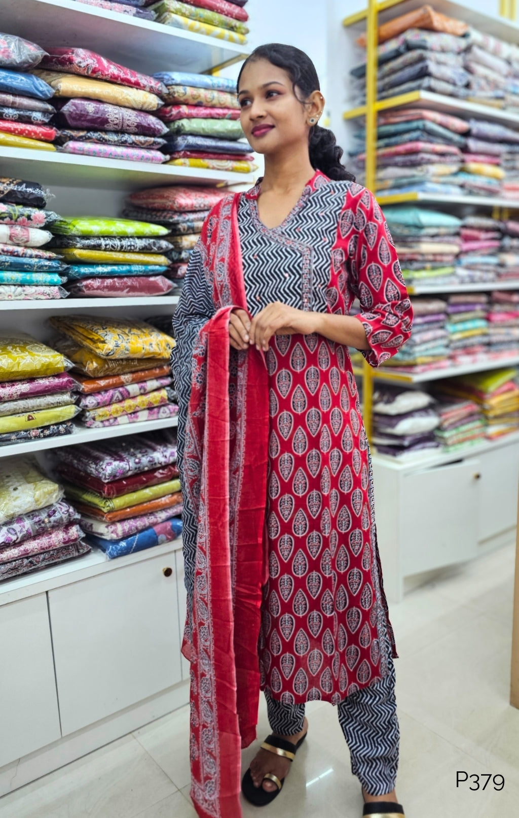 Woman in a patterned outfit standing in a fabric store with shelves of colorful fabrics.
