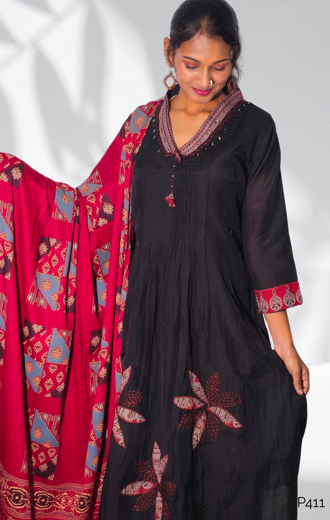 Woman wearing a black outfit with red and blue patterns, standing next to a red and blue patterned fabric on a white background.