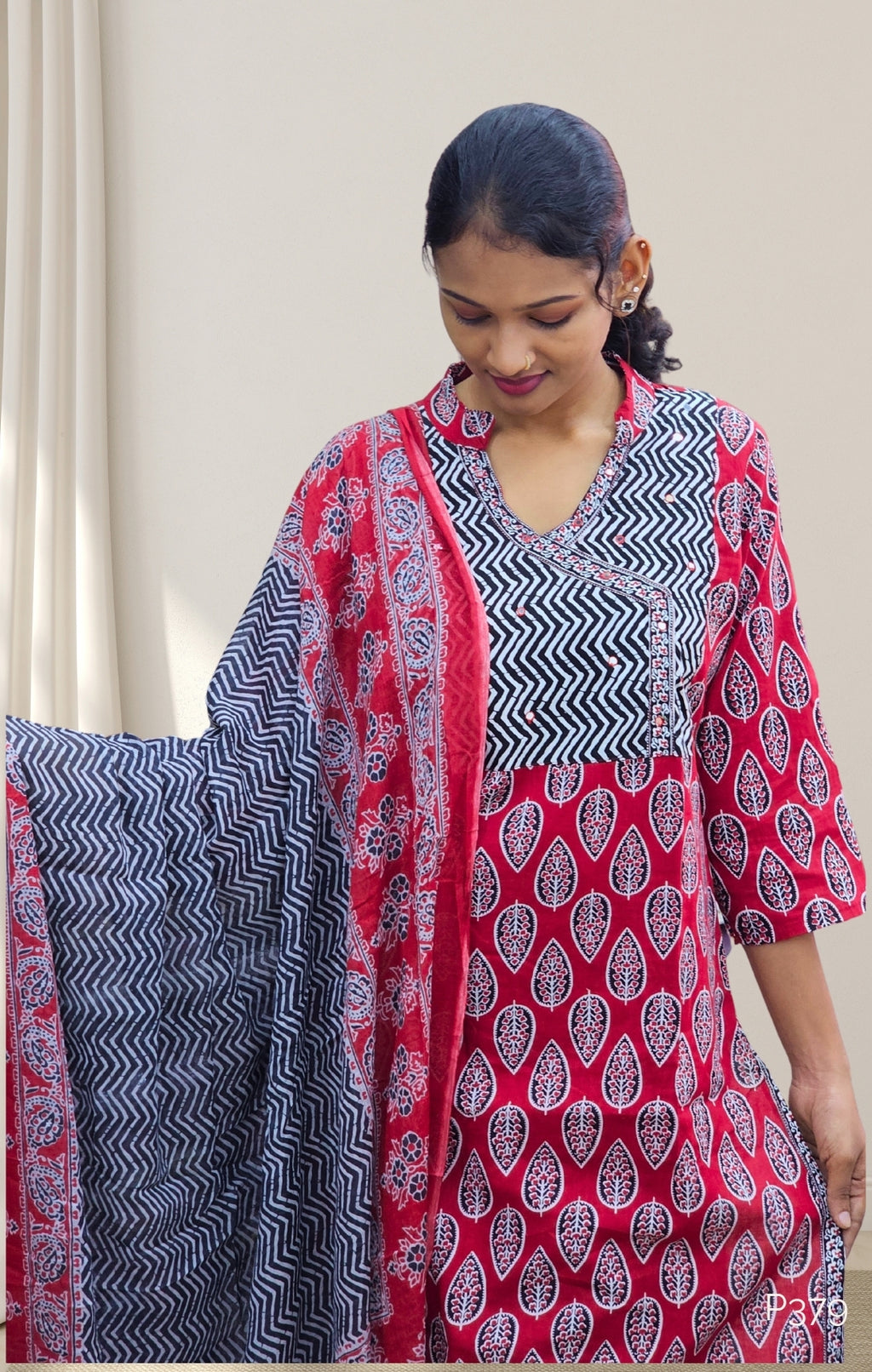 Woman wearing a red and black patterned outfit with a matching shawl indoors.