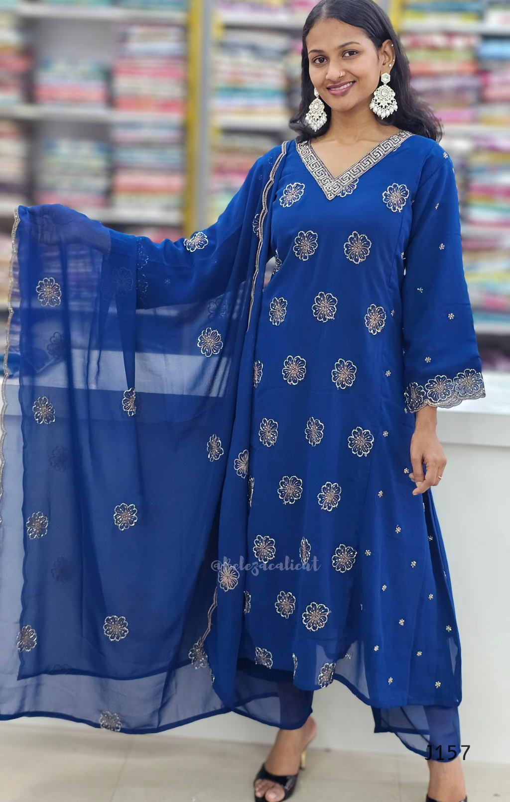 Woman wearing a blue traditional outfit with floral patterns indoors.