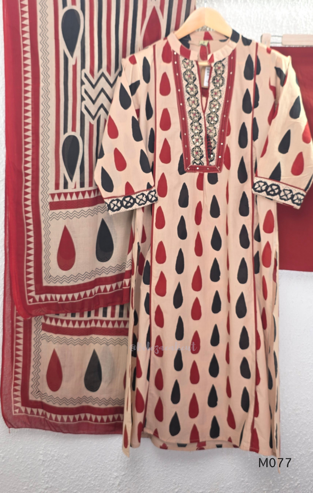 Beige cotton churidar set with red and black teardrop print, embroidered neckline, contrast red bottom and printed dupatta.