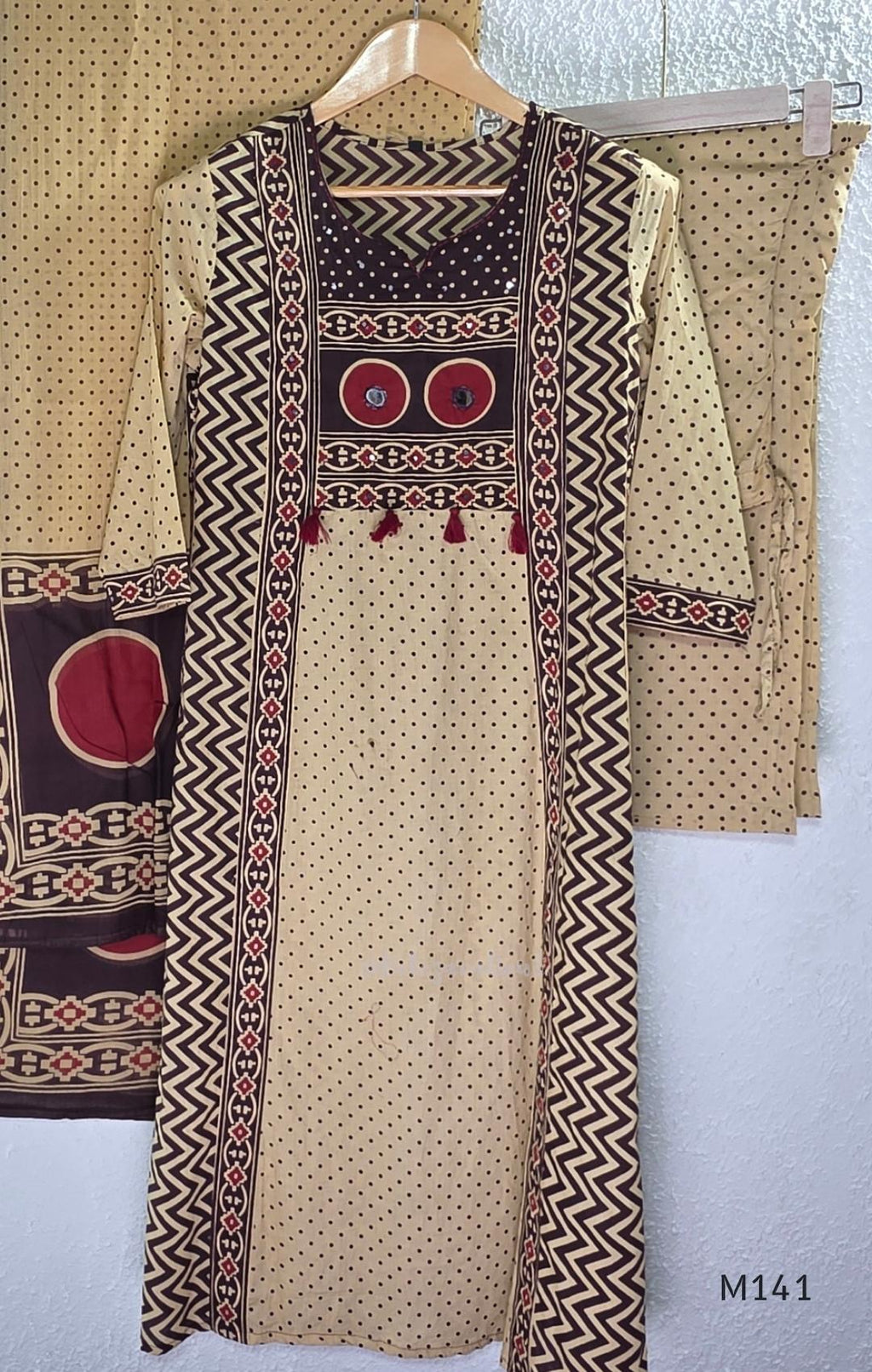 Beige cotton churidar set with dark brown geometric print, red accents, mirror-work yoke, tassels and coordinated dupatta.