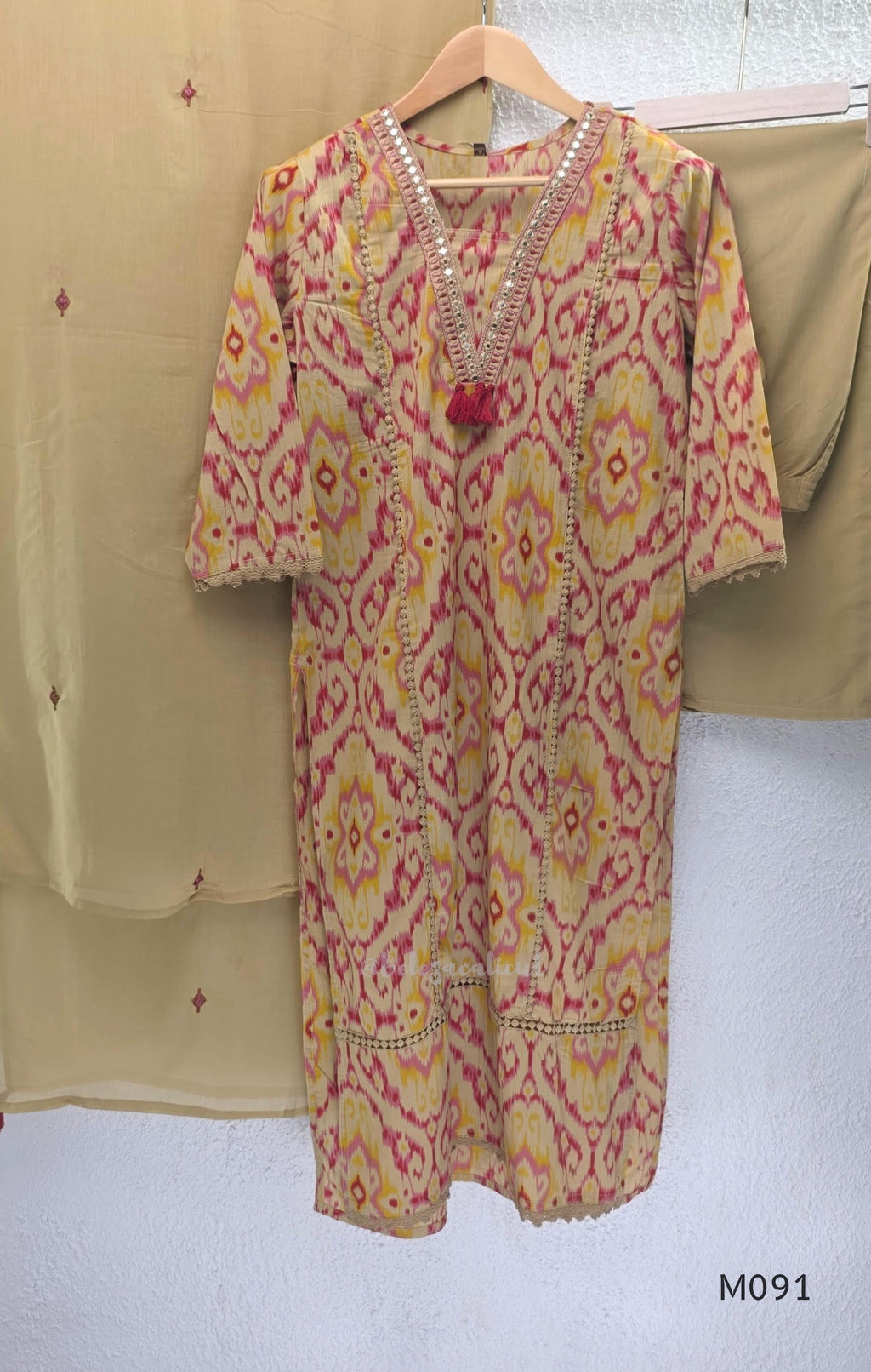Warm beige cotton 3-piece churidar set with pink and mustard ikat-style print, mirror-trimmed V-neck, plain beige bottom and matching dupatta.