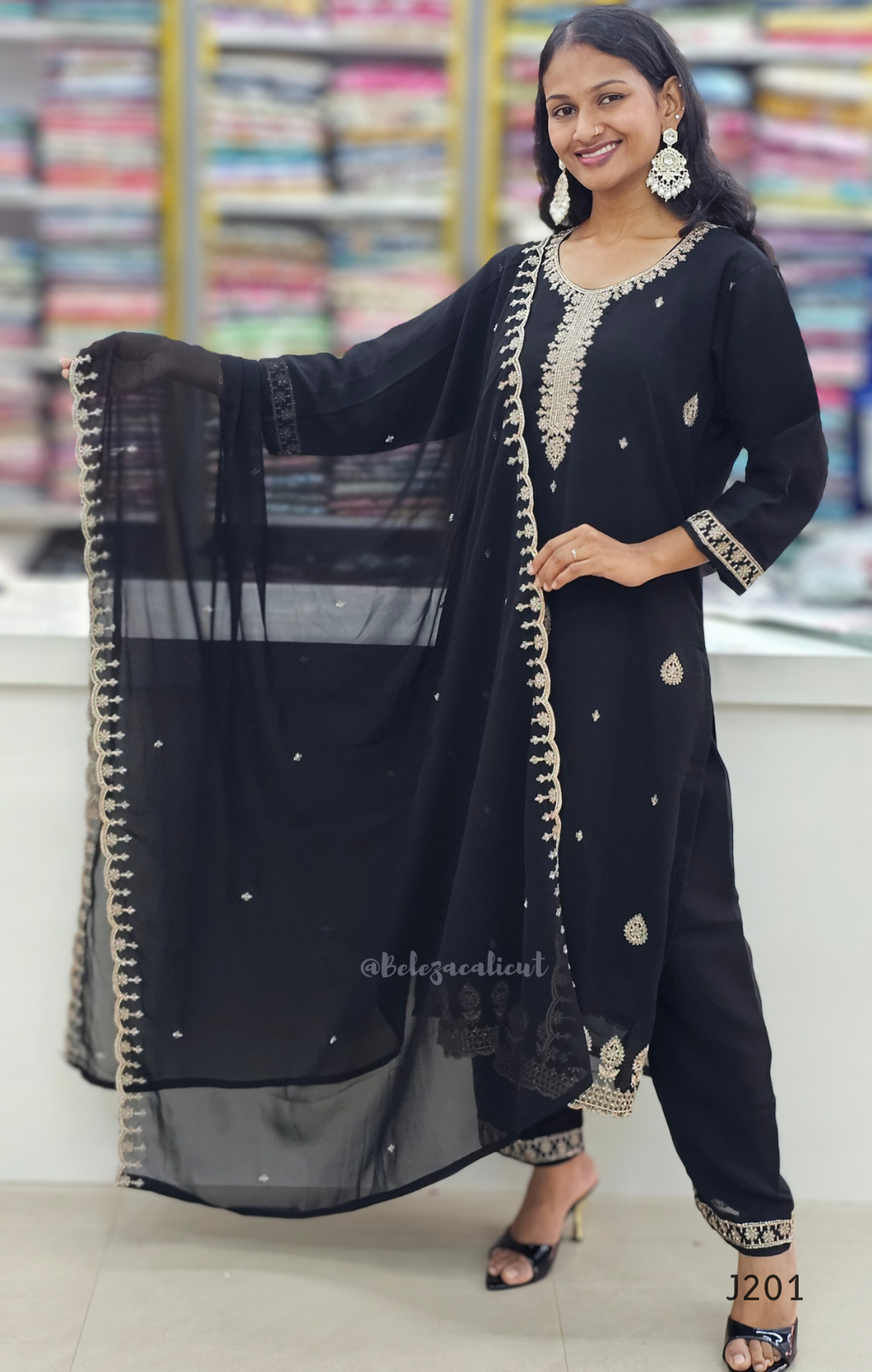 Woman wearing a black traditional outfit with gold embroidery in a store setting.