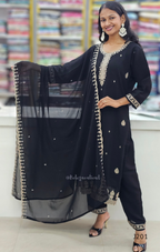 Woman wearing a black traditional outfit with gold embroidery in a store setting.