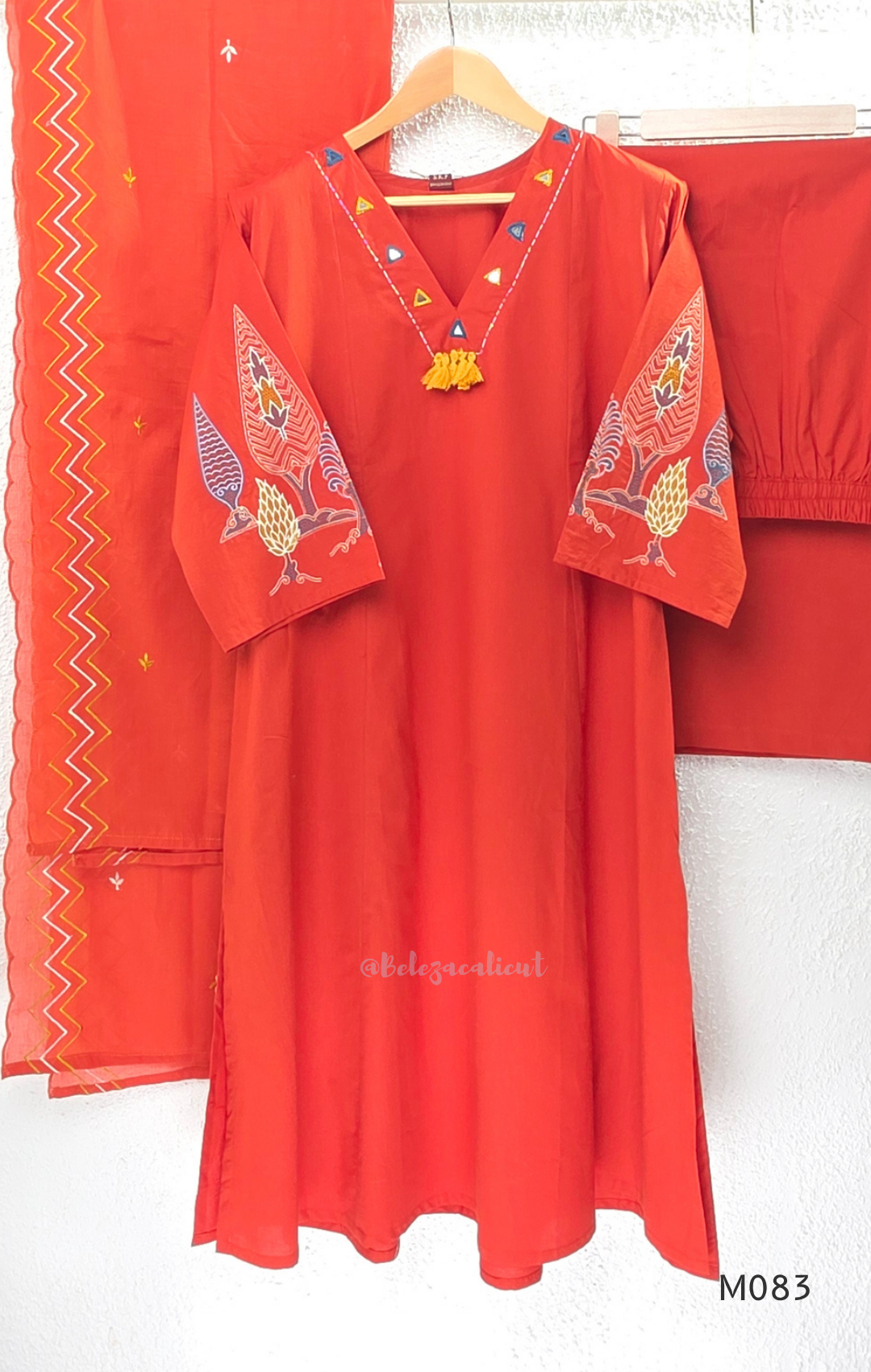Bright orange cotton plus size churidar set with tassel V-neck, embroidered sleeve detail, matching bottom and dupatta.