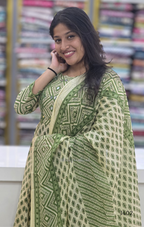 Woman wearing a green and white patterned outfit with a blurred background of books.