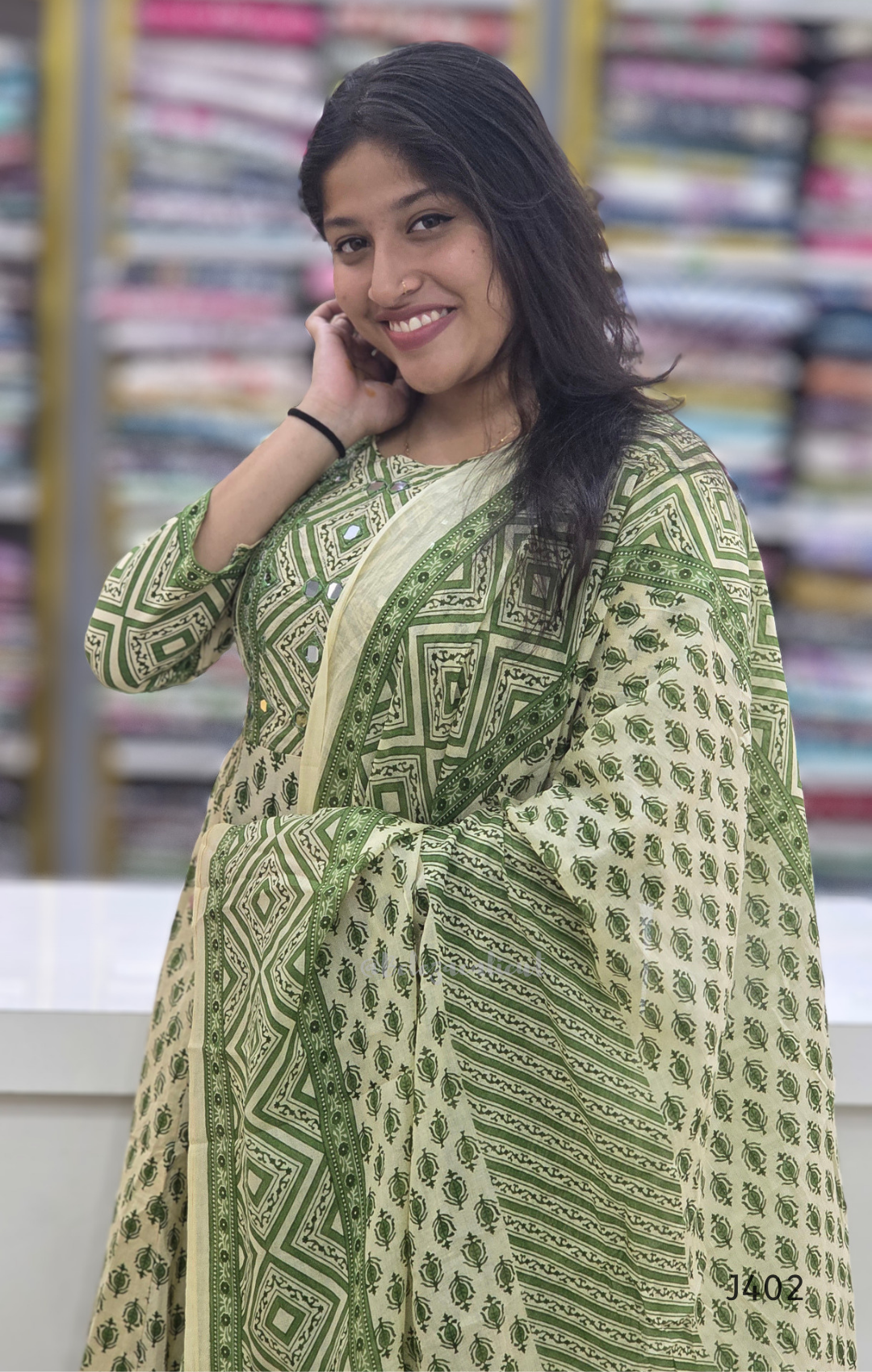 Woman wearing a green and white patterned outfit with a blurred background of books.