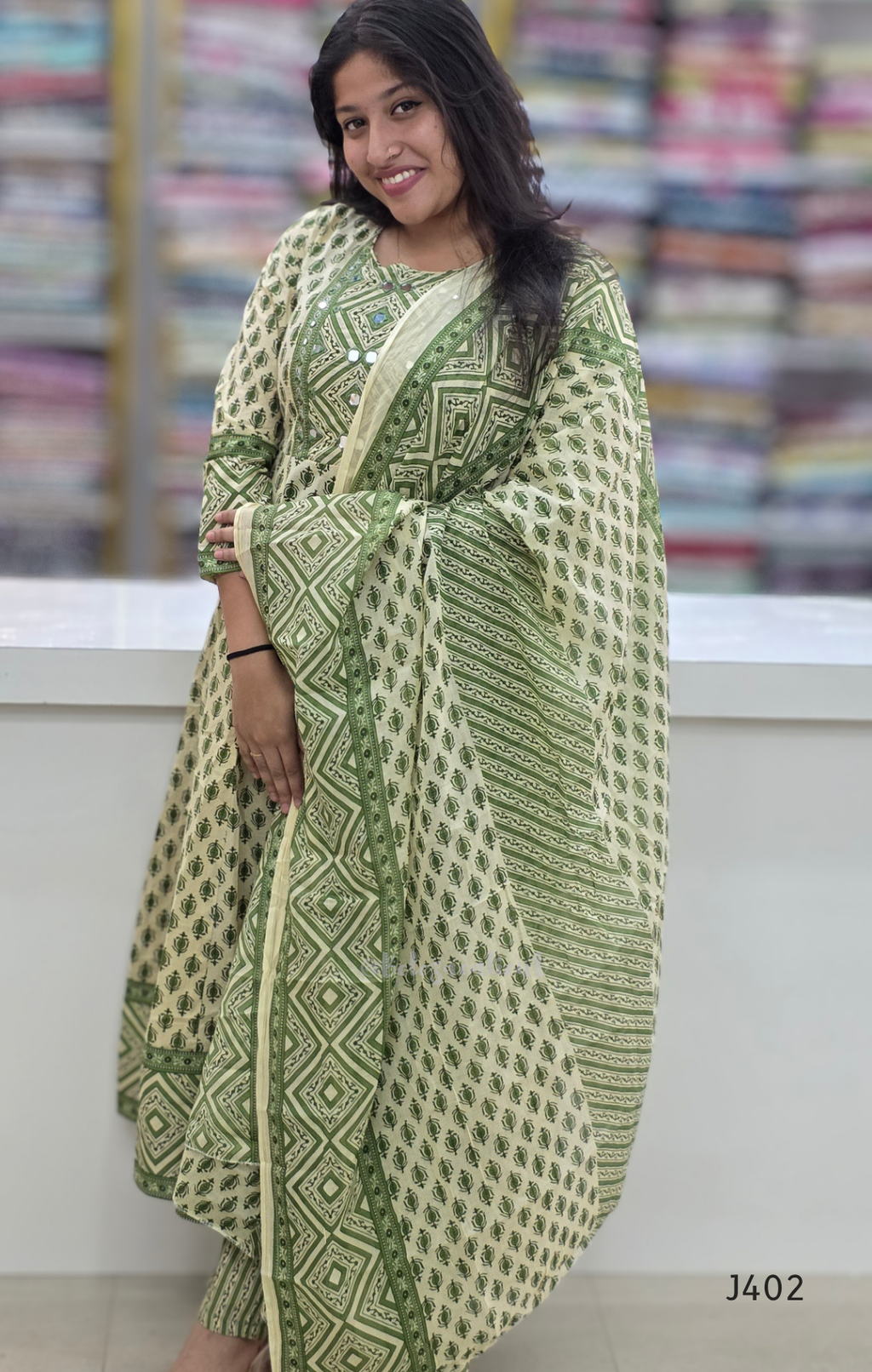 Woman wearing a green and white patterned dress with a blurred fabric background