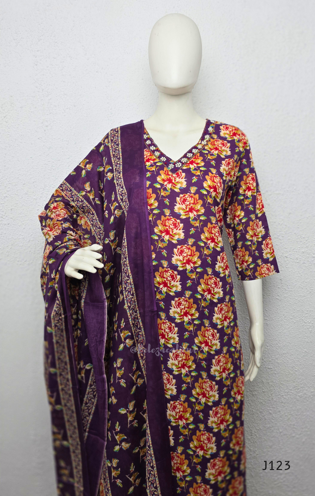 Deep purple cotton churidar set with rose floral print, matching dupatta, 3/4 sleeves, and embellished V-neckline displayed on mannequin.