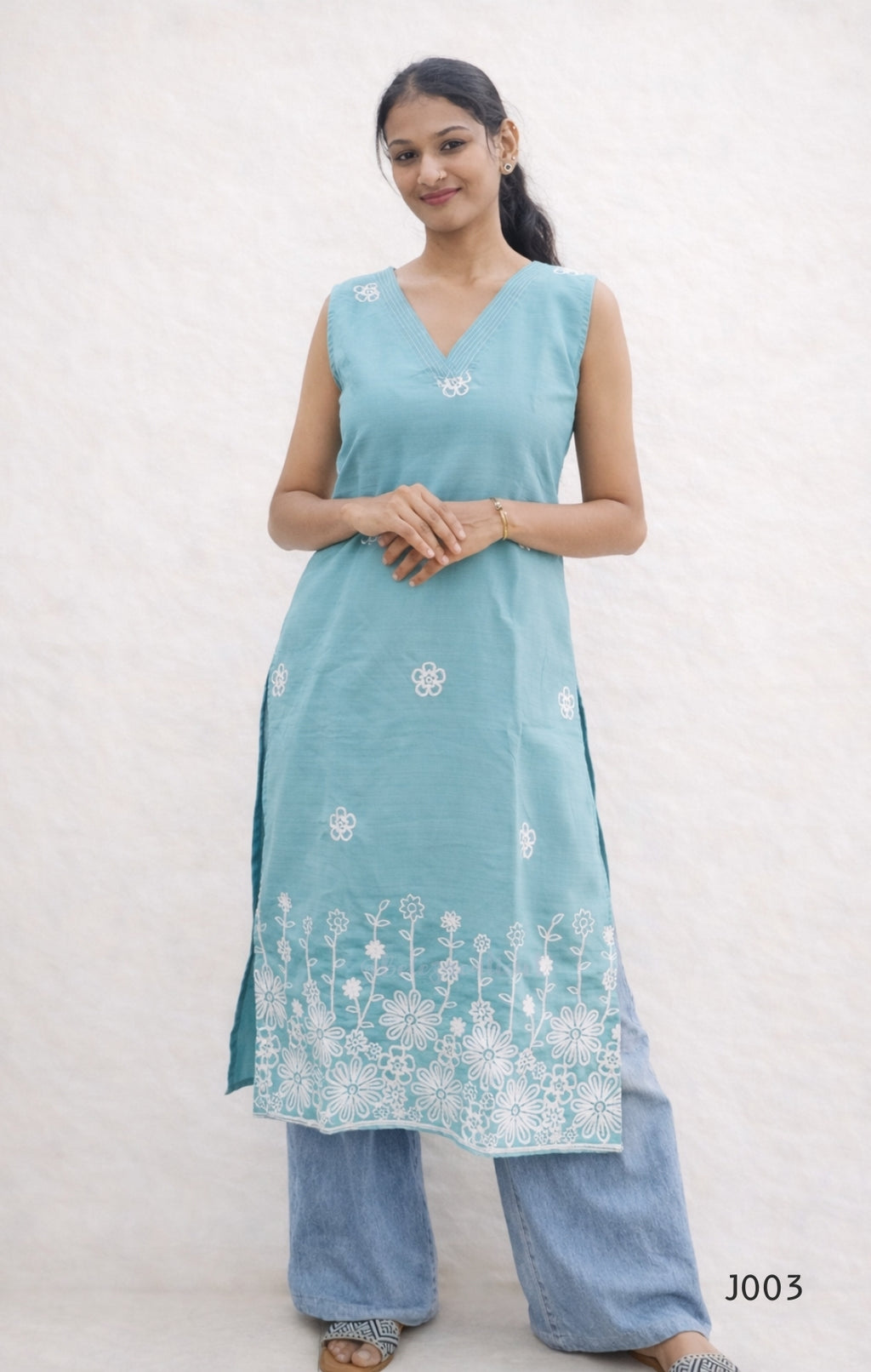 Woman wearing a light blue sleeveless kurta with white floral embroidery on a plain background