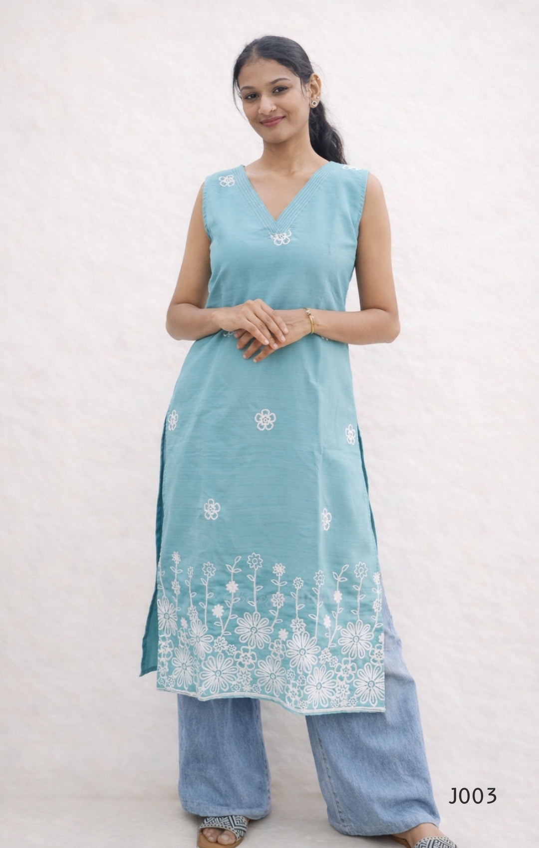 Woman wearing a light blue sleeveless kurta with white floral embroidery on a plain background