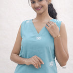 Woman wearing a light blue sleeveless top with white floral embroidery on a plain background