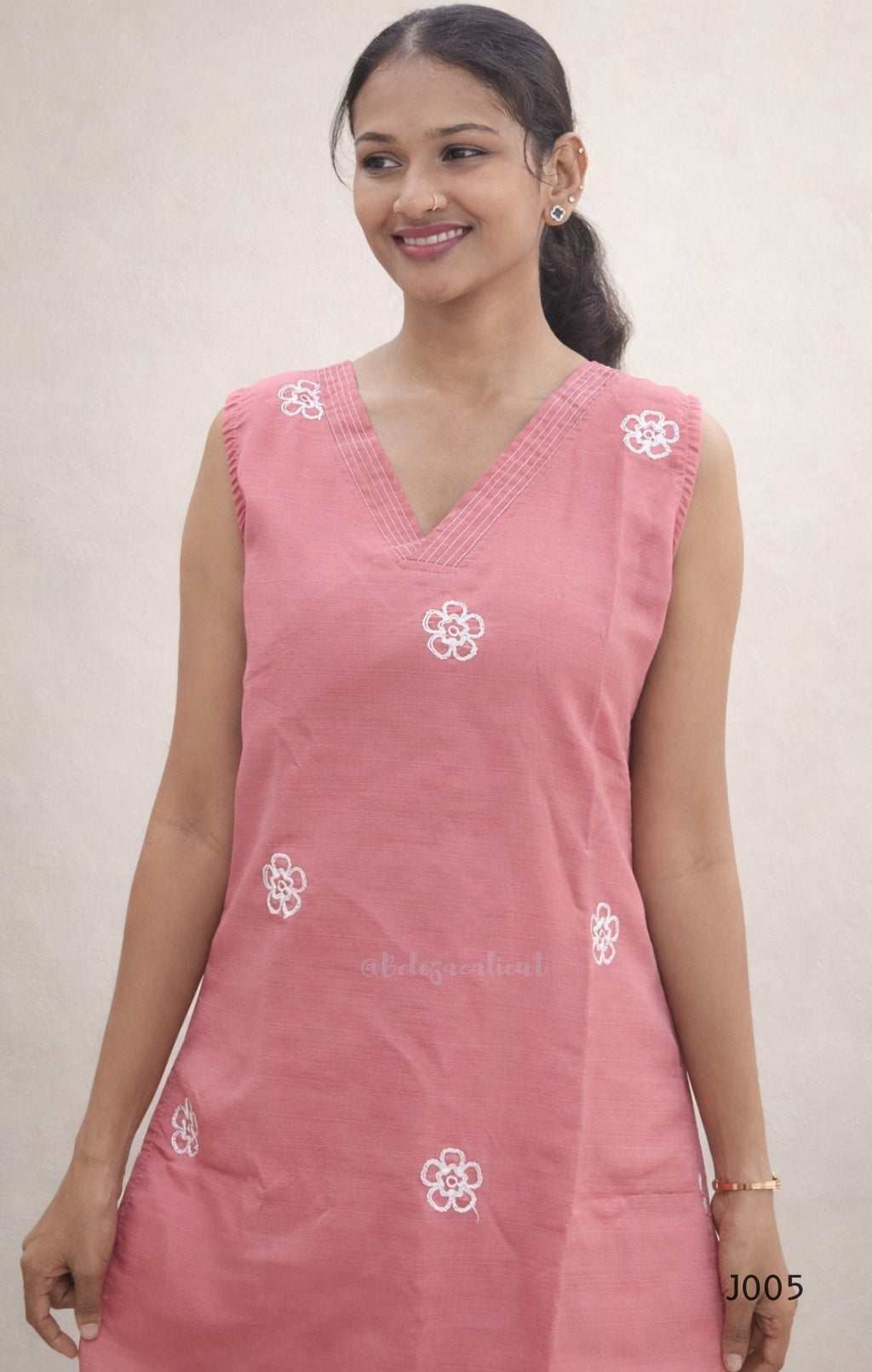 Woman wearing a pink sleeveless top with white floral patterns on a plain background