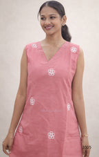 Woman wearing a pink sleeveless top with white floral patterns on a plain background
