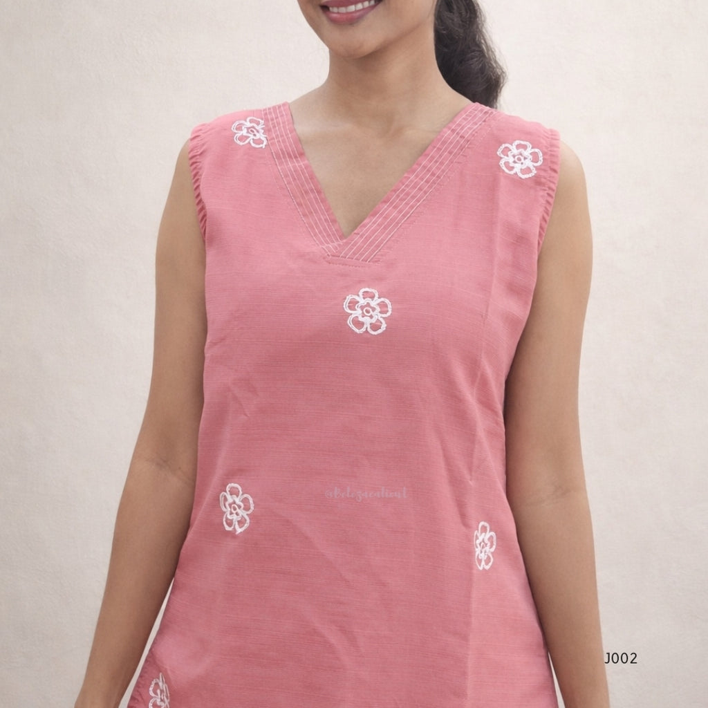 Woman wearing a pink sleeveless top with white floral embroidery on a plain background