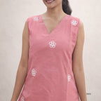 Woman wearing a pink sleeveless top with white floral embroidery on a plain background