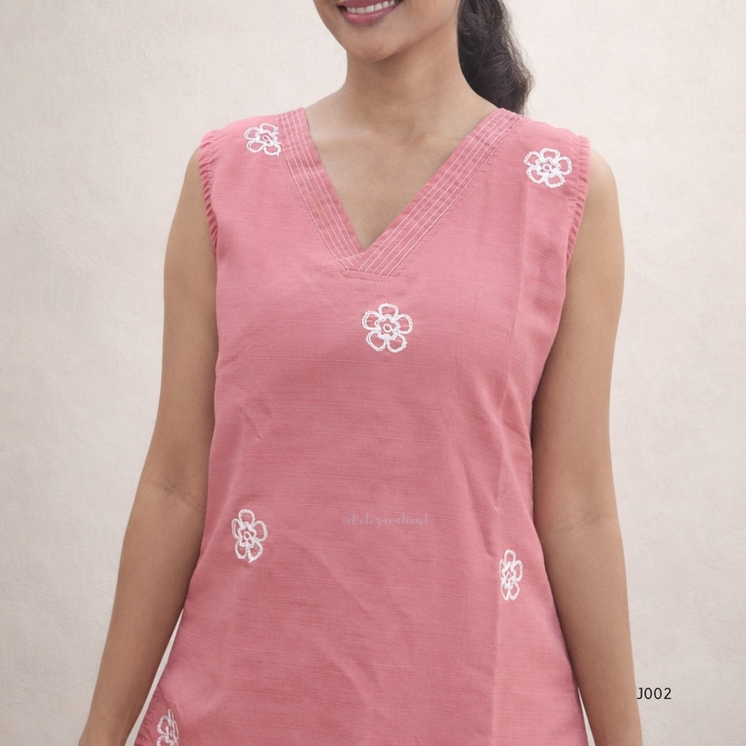 Woman wearing a pink sleeveless top with white floral embroidery on a plain background