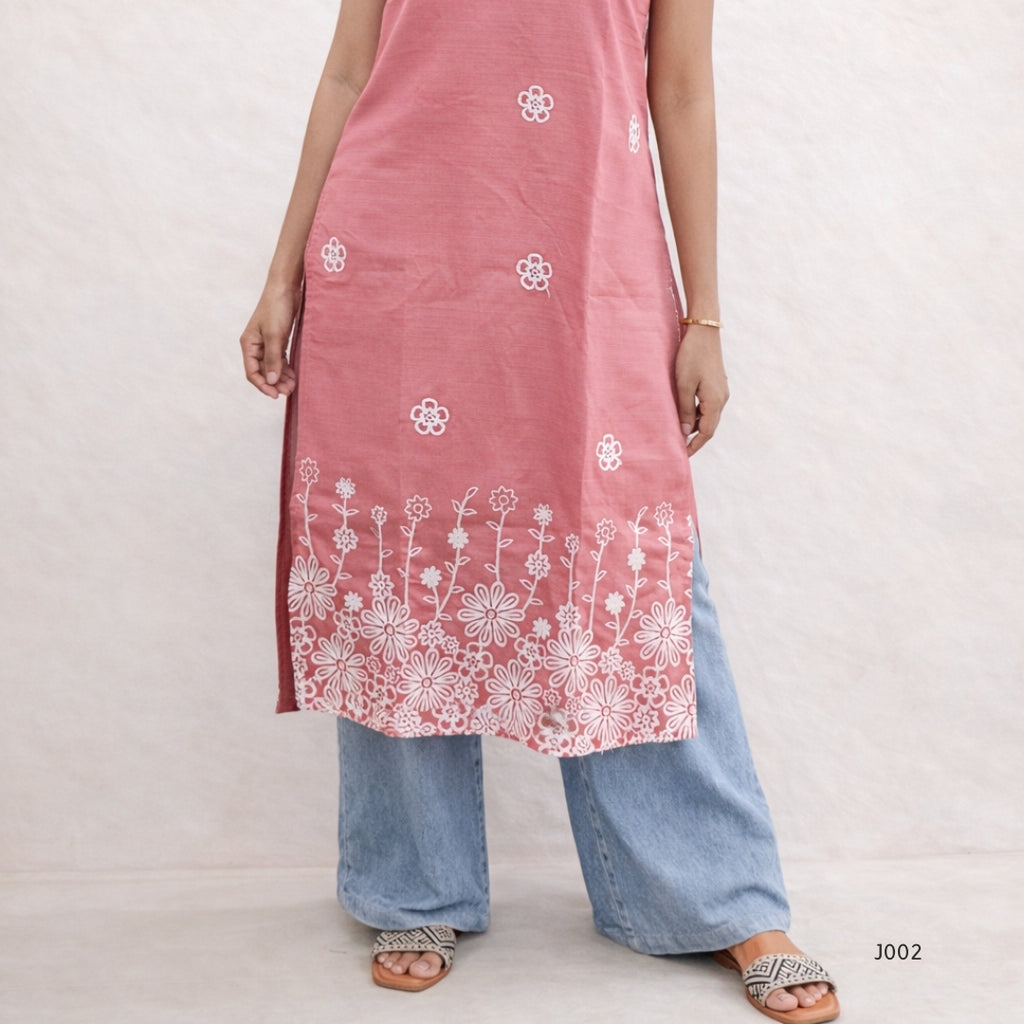 Person wearing a pink embroidered dress with white floral patterns on a plain background