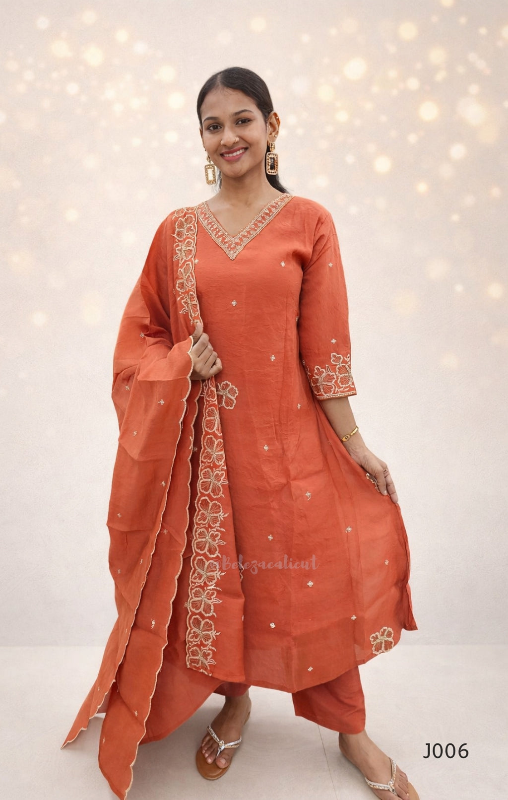 Woman wearing an orange traditional outfit with intricate embroidery against a light background