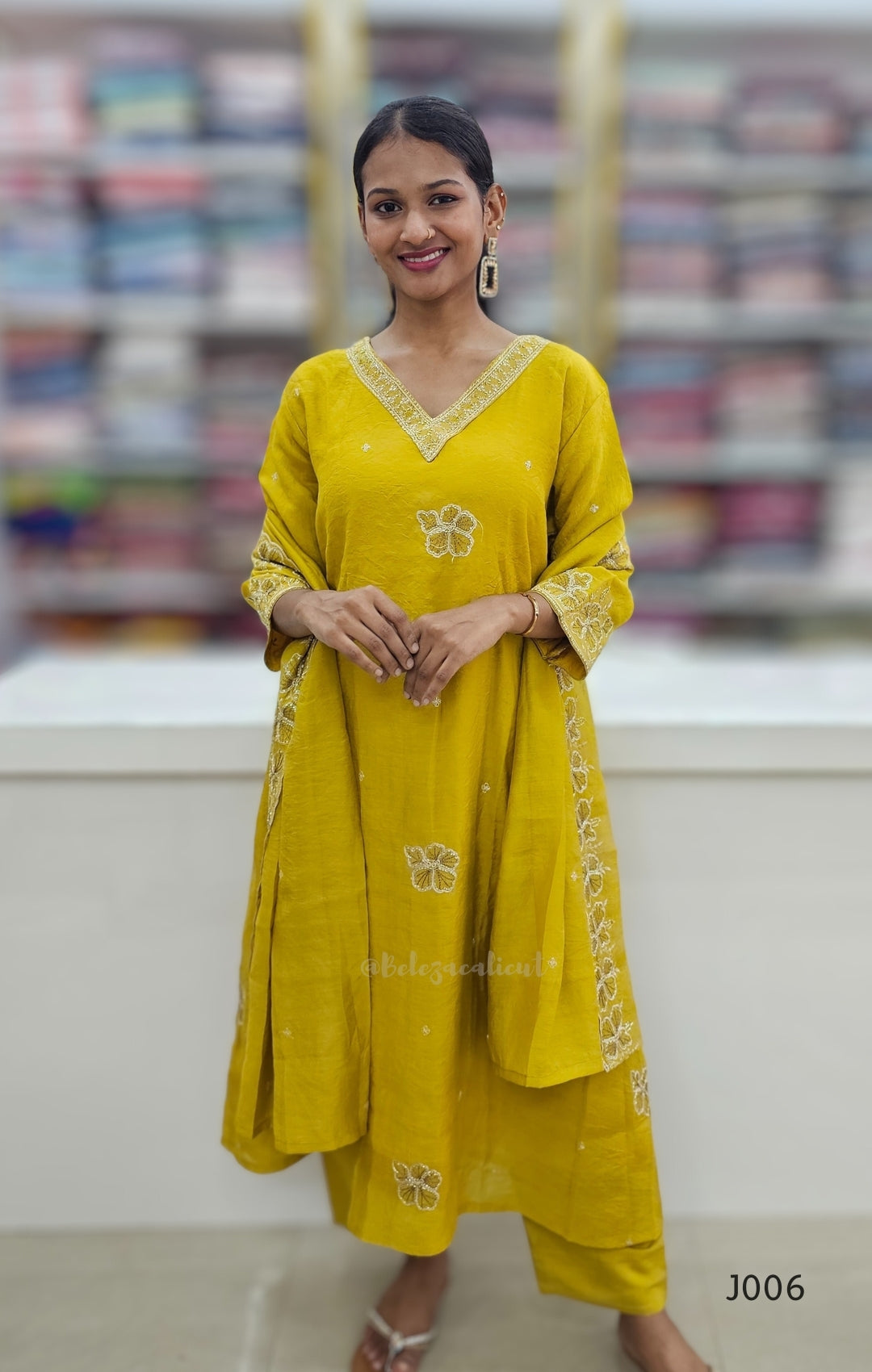 Woman wearing a yellow traditional outfit with floral patterns in an indoor setting.