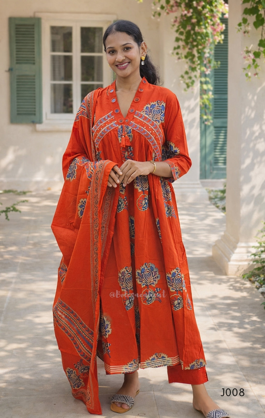 Woman wearing an orange traditional outfit with intricate patterns in a garden setting.