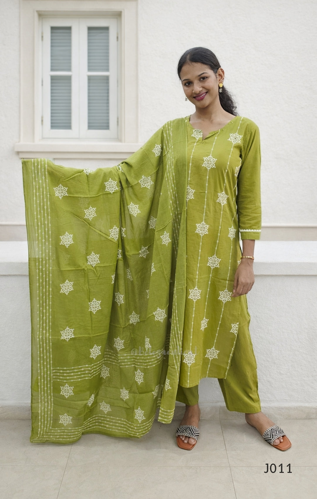 Woman wearing a green traditional outfit with a matching dupatta in front of a white wall.