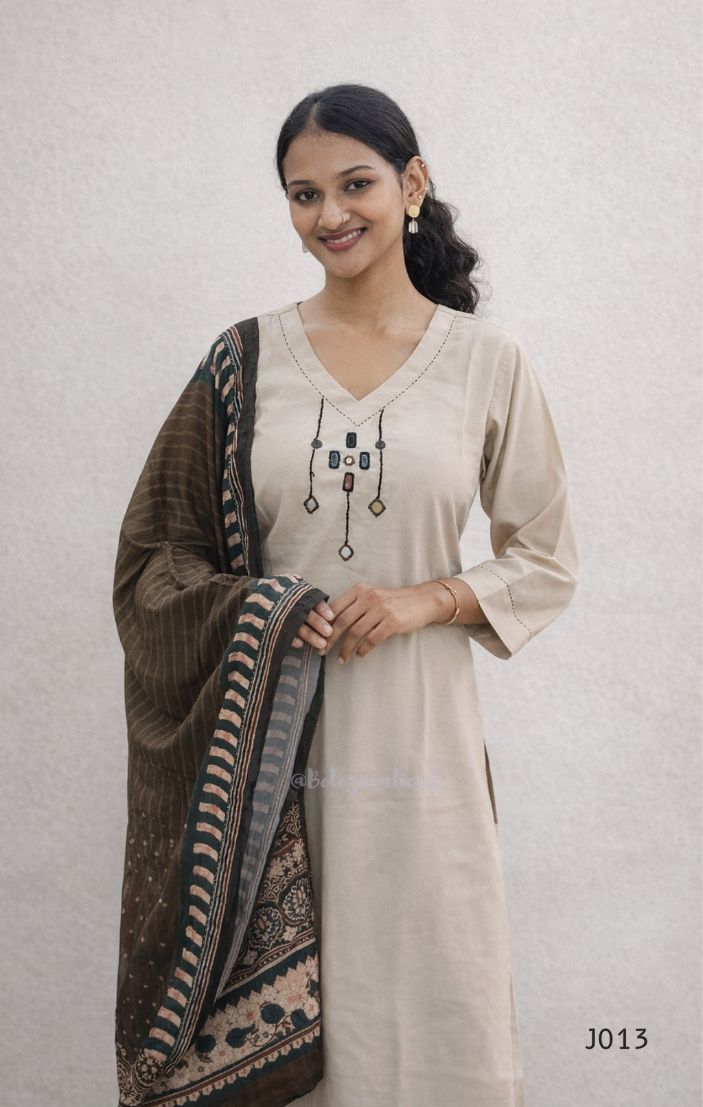 Woman wearing a beige kurta with a brown and black patterned dupatta on a light gray background