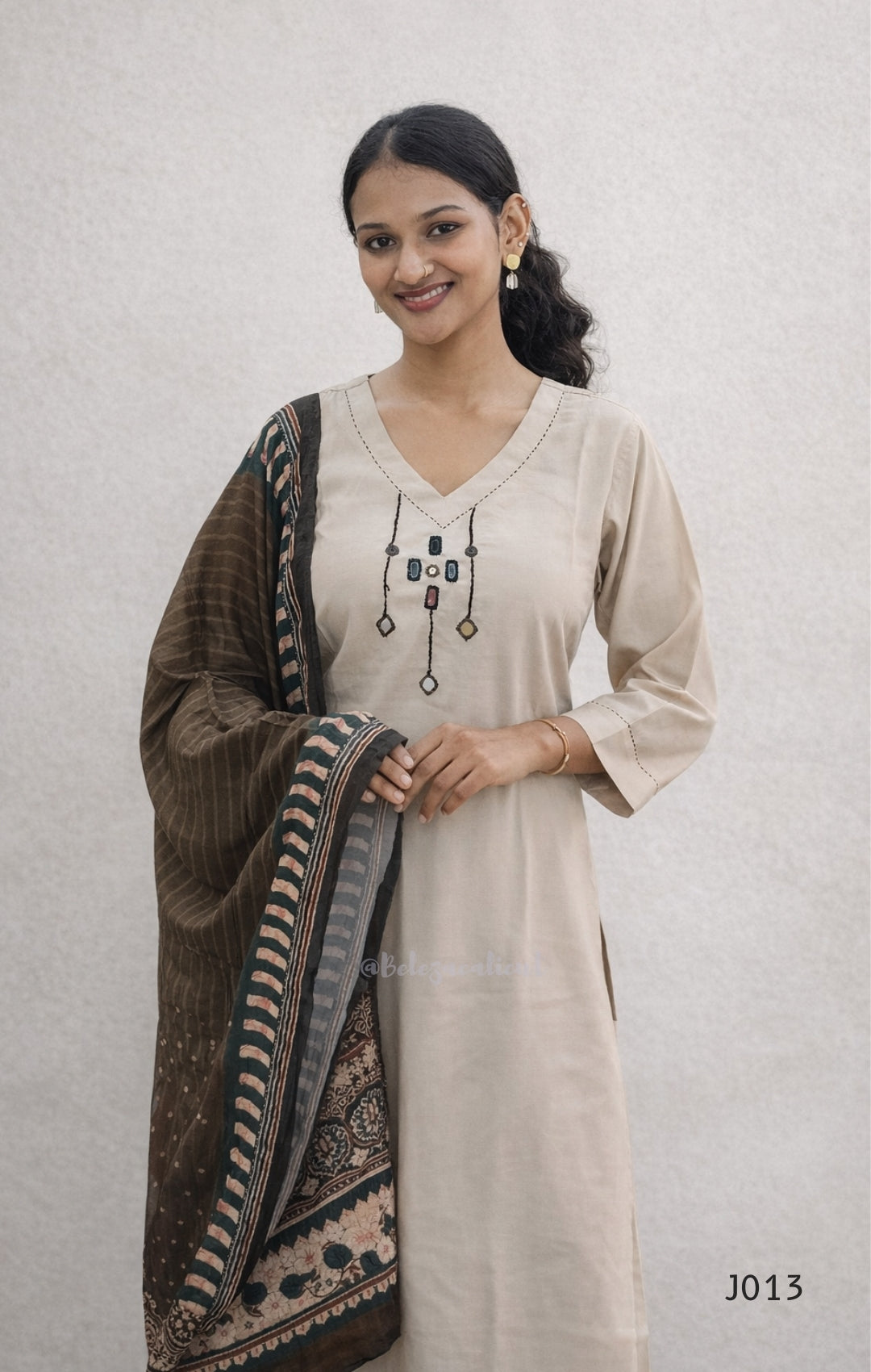 Woman wearing a beige kurta with a brown and black patterned dupatta on a light gray background