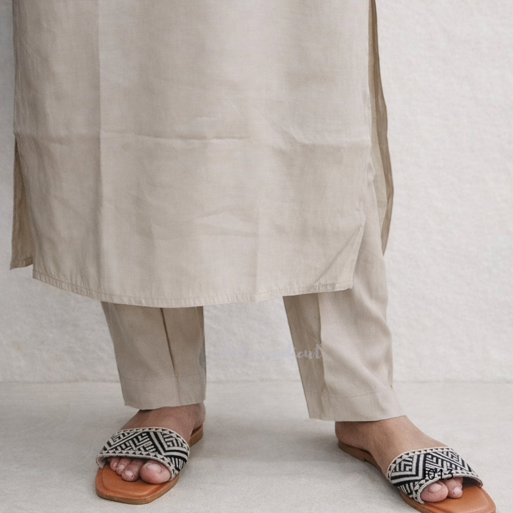 Person wearing beige pants and patterned sandals on a light background