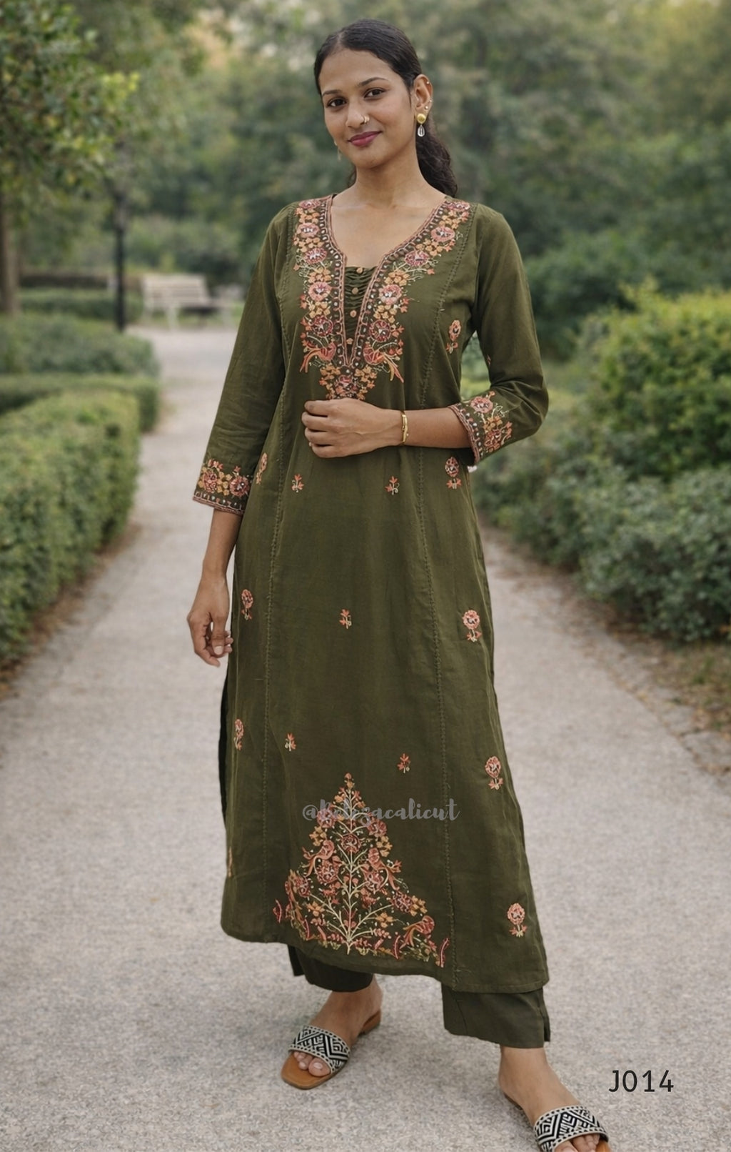 Woman wearing a green embroidered traditional outfit standing outdoors.