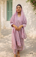 Woman in a pink traditional outfit standing outdoors with a building and greenery in the background.