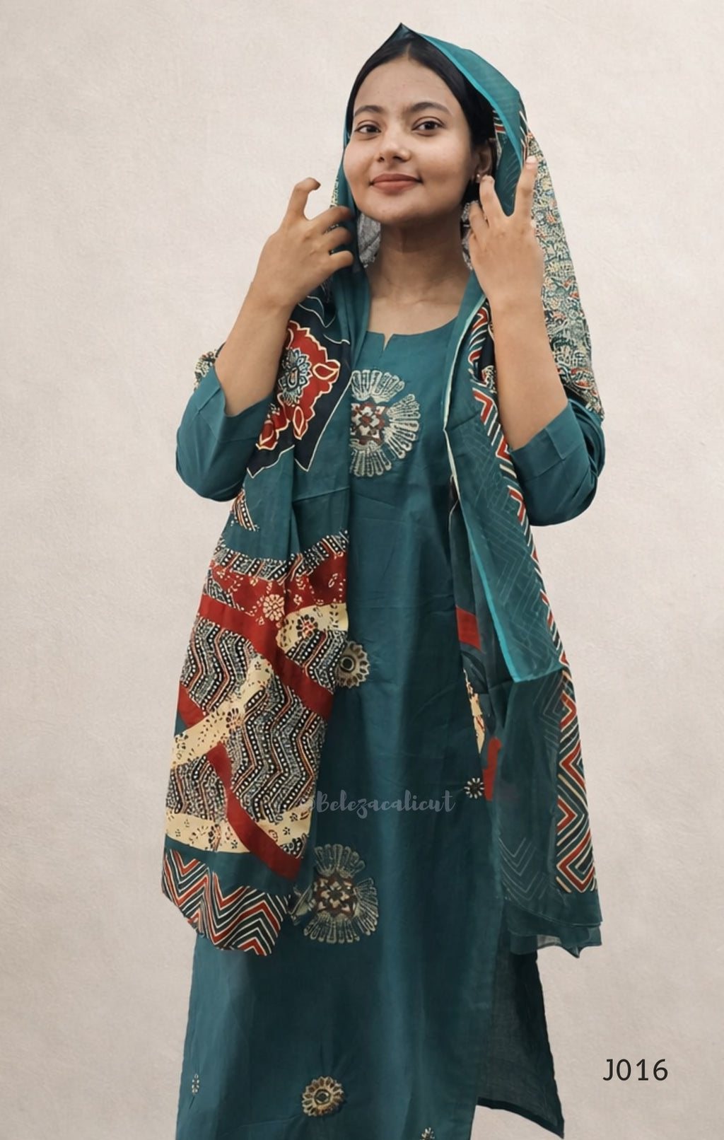 Woman wearing a teal outfit with a patterned shawl against a plain background