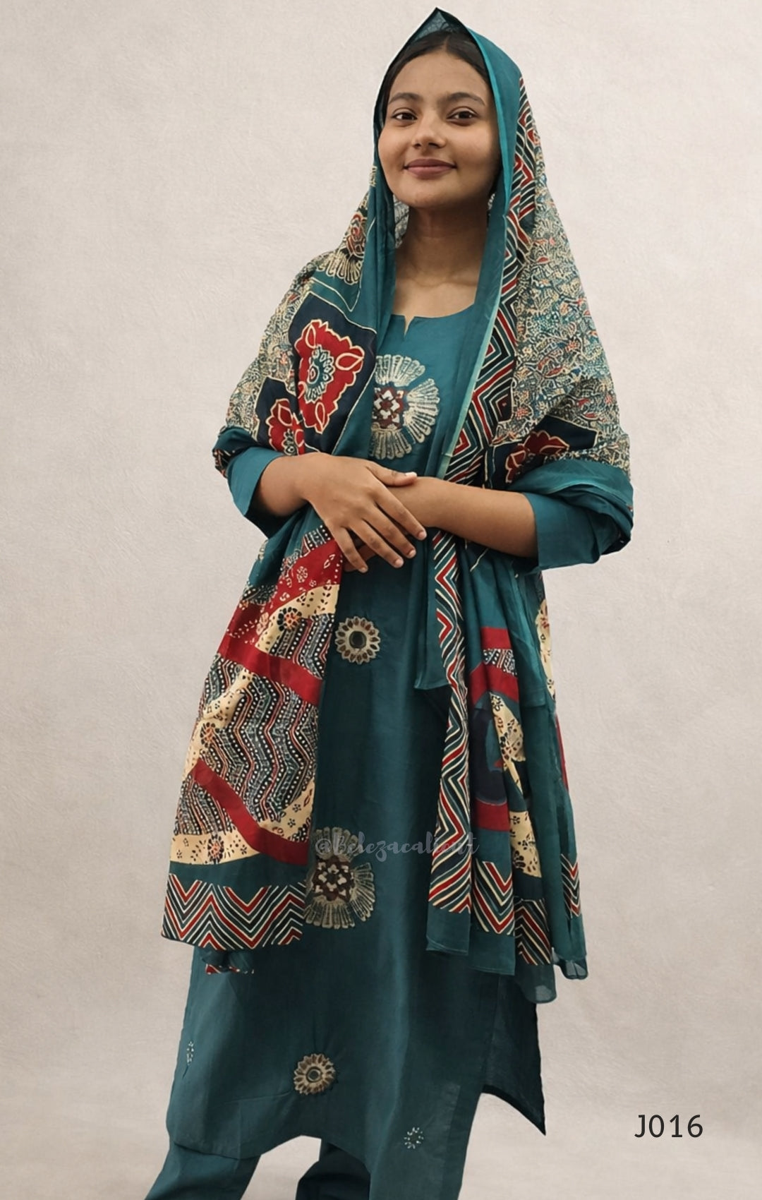 Woman wearing a teal outfit with a patterned shawl on a plain background