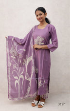 Woman wearing a purple outfit with a floral scarf on a plain background