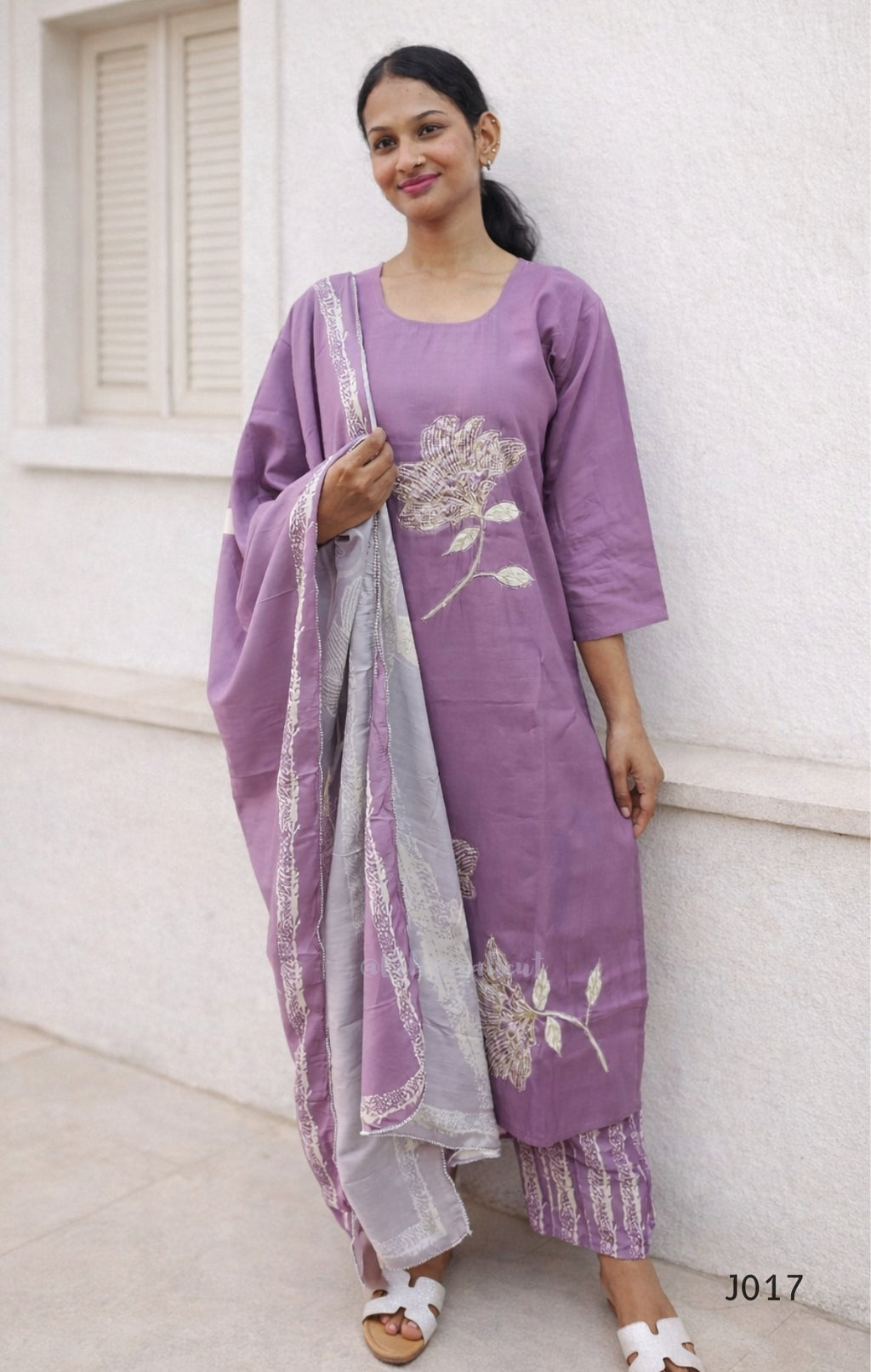 Woman wearing a purple outfit with floral patterns against a white wall.