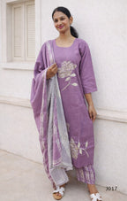 Woman wearing a purple outfit with floral patterns against a white wall.
