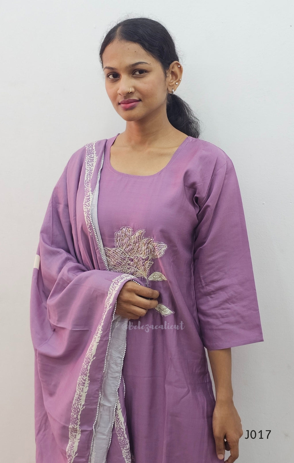 Woman wearing a purple traditional outfit with white embroidery on a plain background