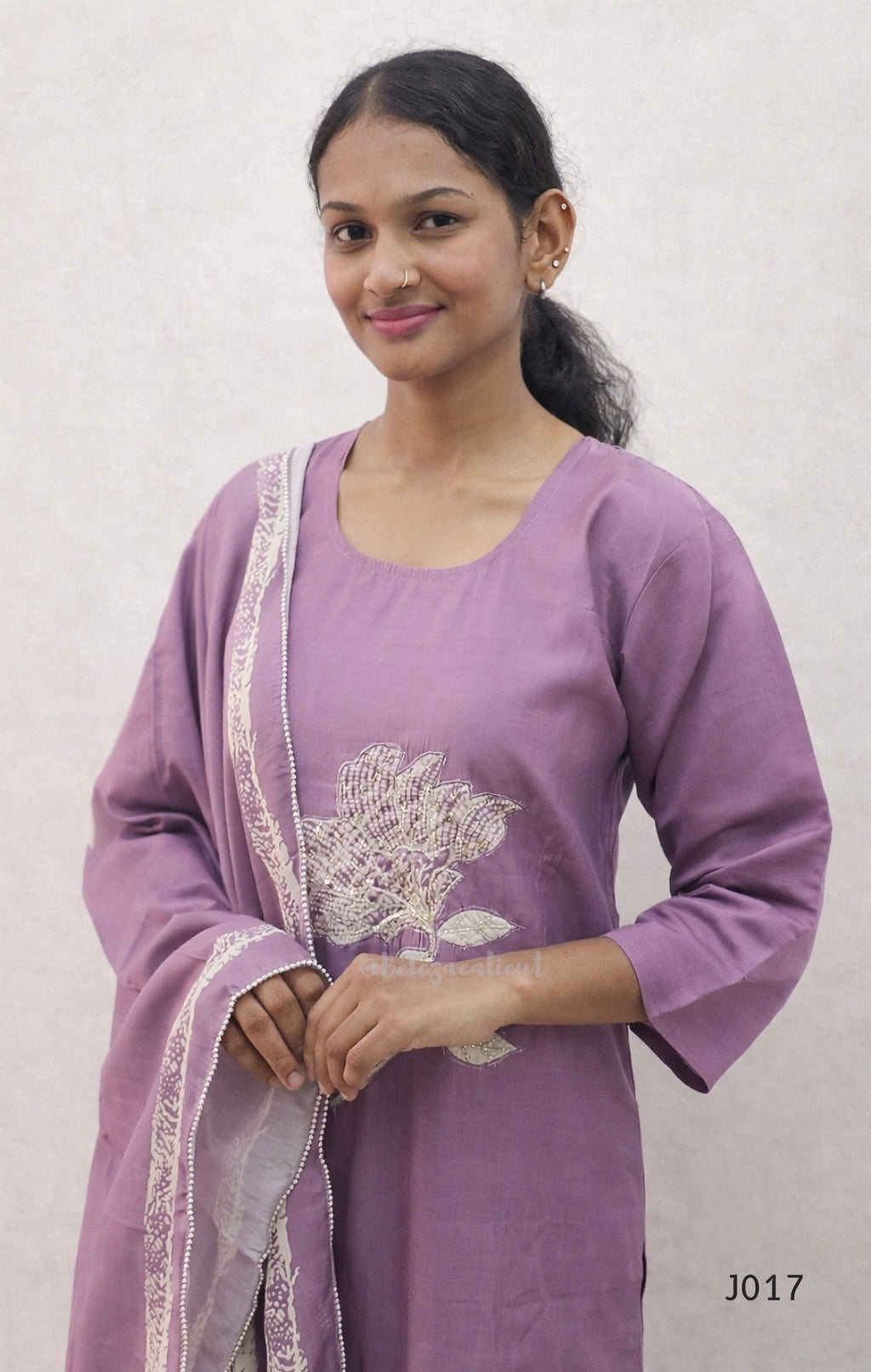 Woman wearing a purple traditional outfit with a white floral design on a plain background
