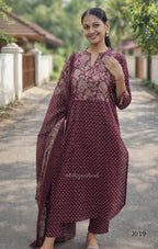 Woman wearing a maroon traditional outfit with floral patterns outdoors.