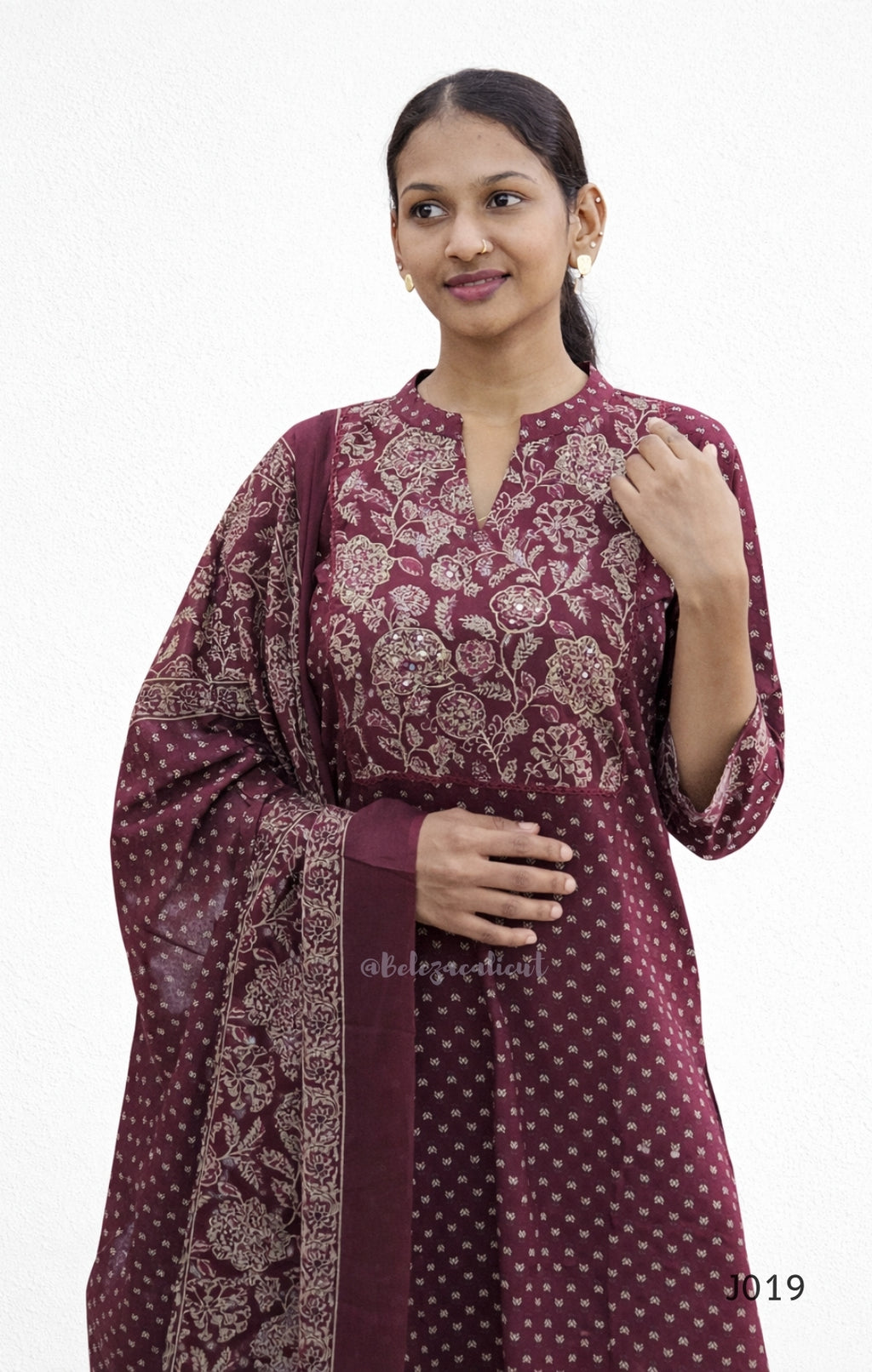 Woman wearing a maroon traditional outfit with floral patterns on a white background