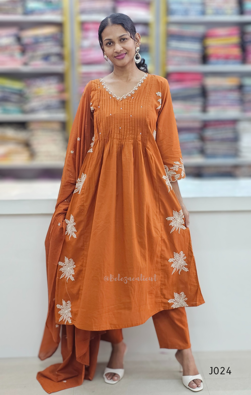 Woman wearing an orange traditional outfit with white floral patterns in a store setting.