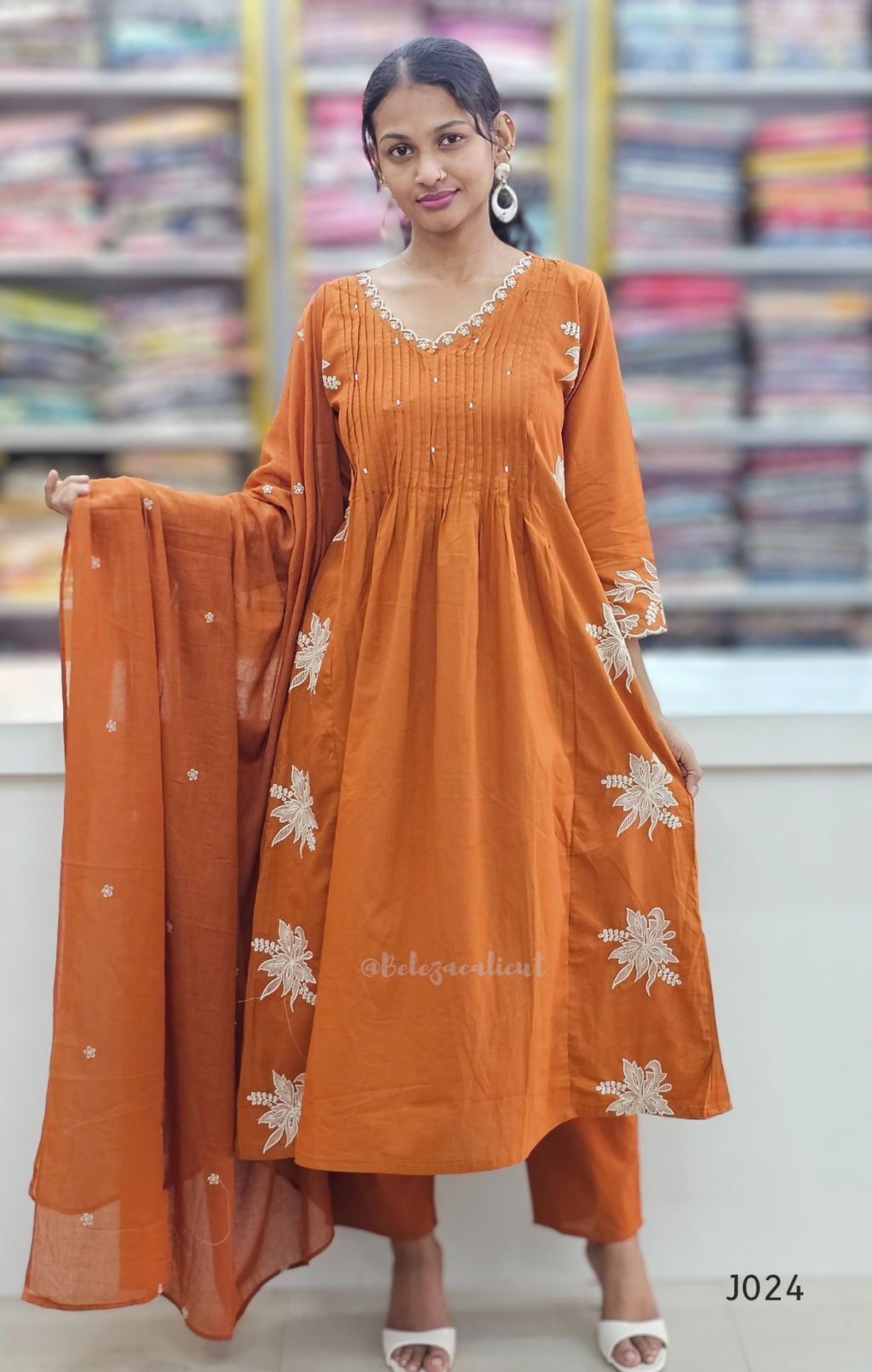 Woman wearing an orange traditional outfit with white floral patterns in a store setting.