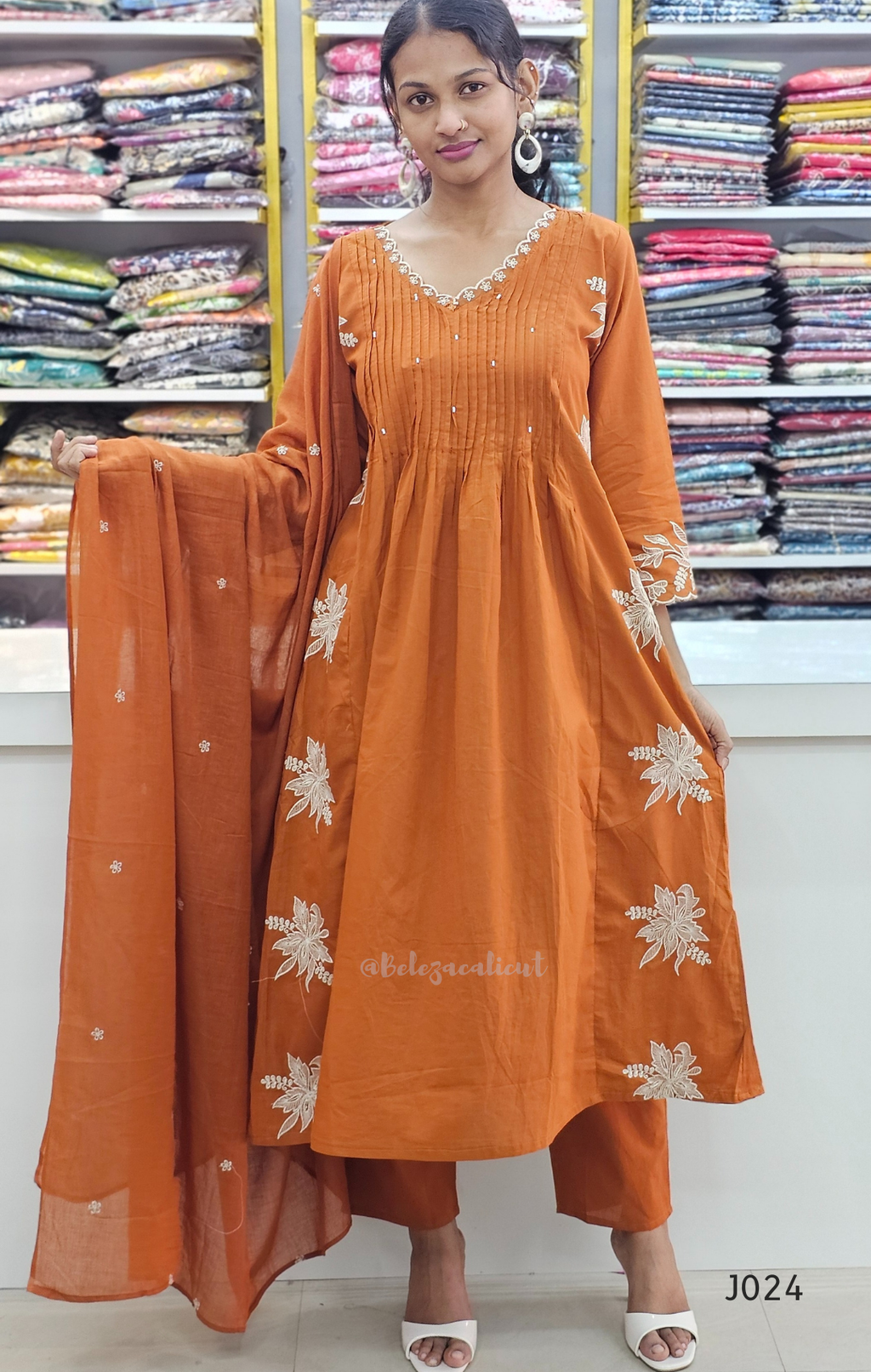 Woman wearing an orange traditional outfit with floral patterns in a fabric store.